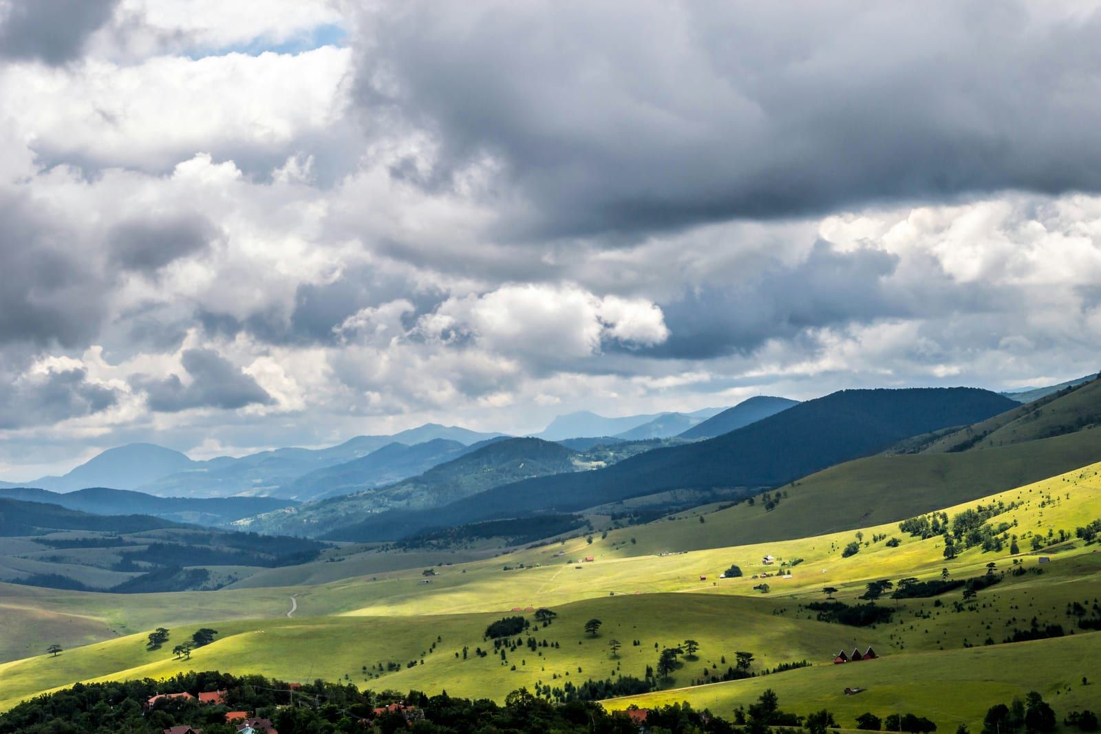 Zelene padine Zlatibora u sunčevim zracima ispod teških oblaka, sa planinskim vencima u pozadini