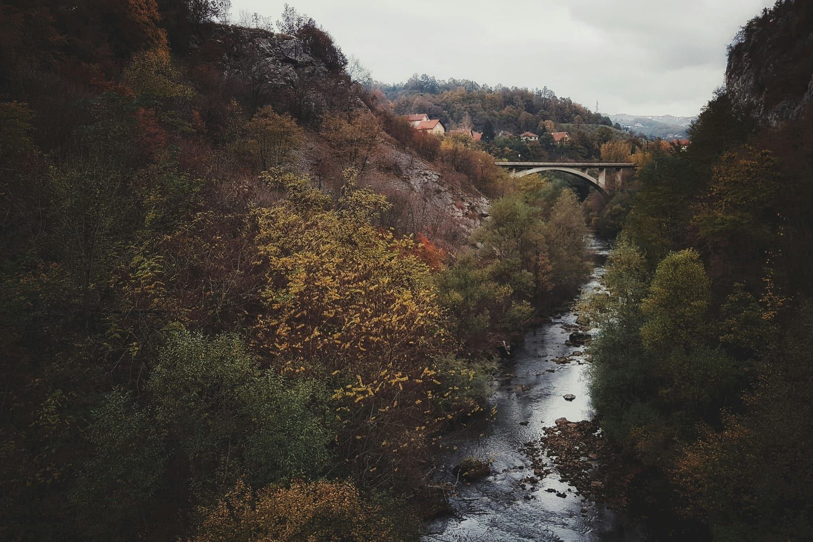 Reka između šumovitih padina sa mostom u daljini, u jesen, kod Užica